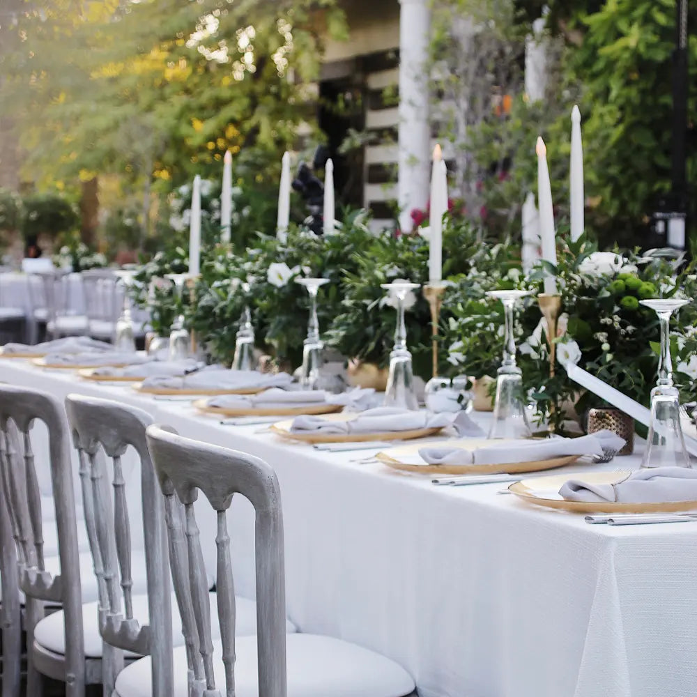 Rectangular Tablecloth Linen Blend elegantly drapes a long dining table, set with greenery, candles, and place settings for an outdoor event.