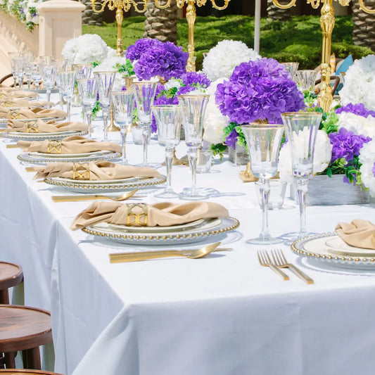 Rectangular Tablecloth Linen Blend elegantly drapes a formal outdoor dining table, featuring gold-edged settings and lush floral arrangements, ideal for sophisticated events.