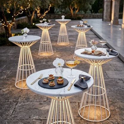 WHITE WIRE COCKTAIL TABLE-WHITE MARBLE TOP amid a cocktail setup, featuring hors d’oeuvres, drinks, and orchids, creating an elegant, illuminated atmosphere for events.