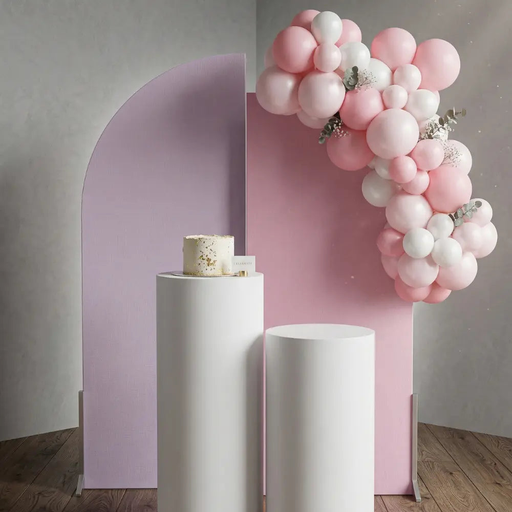White Wood Curved Backdrop with arched panels, white pedestals, minimalist cake, and balloon garland, perfect for elegant party or event displays.