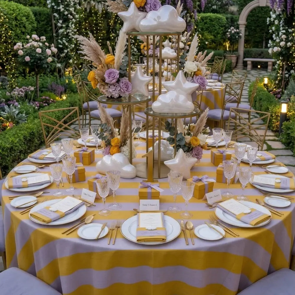 Wide Stripes Round Tablecloth in a garden setting, featuring yellow-and-grey stripes, enhances an elegant outdoor dining setup with fine china and whimsical centerpieces.
