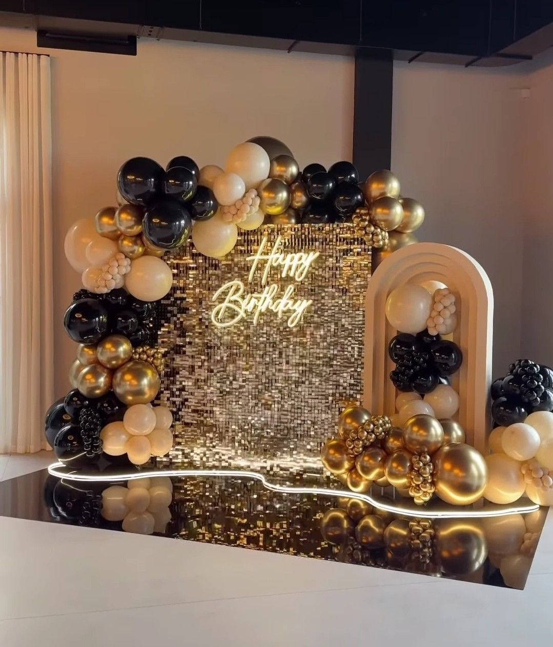 Decorative birthday setup with balloons and a 'Happy Birthday' sign on a reflective surface.