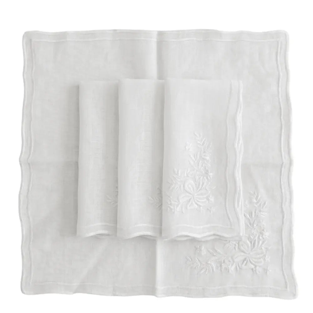 Set of four white linen dinner napkins with floral embroidery and scalloped edges, enhancing elegant table settings.
