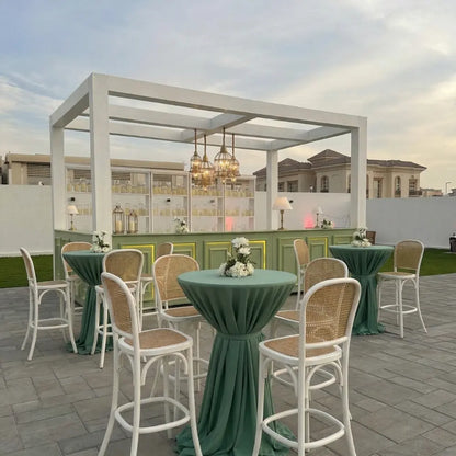 Wood Rattan Stool with woven cane seat and back, set around cocktail tables in an elegant outdoor lounge setup, perfect for event rentals.