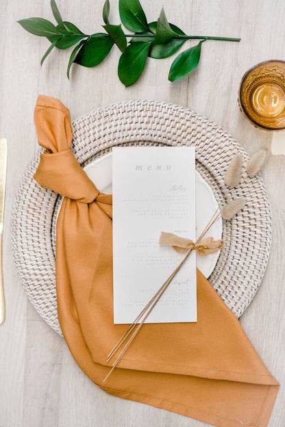 Charger Plate - Rattan on a set table with a napkin and menu, enhancing a rustic or boho-themed event setting.