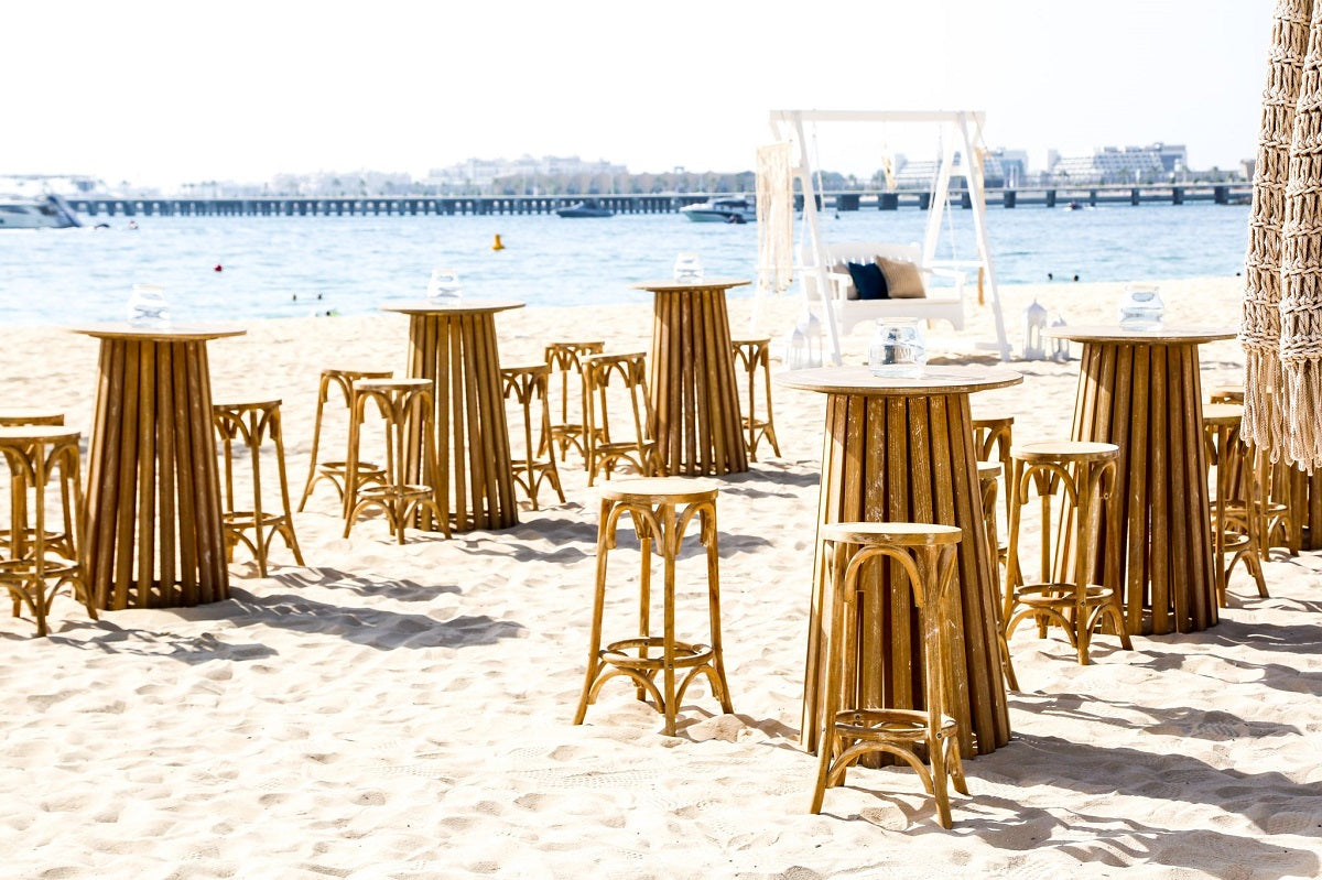 Wooden Bar Stool set on a beach, ideal for weddings and events, showcasing its classic oak design and versatility for outdoor use.