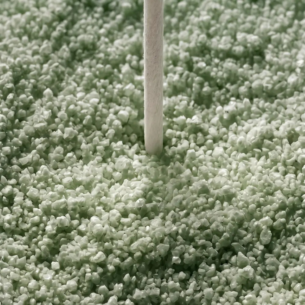 A close-up of a light sage green shag carpet with a single white stick or stick-like object standing upright in the center.