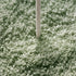 A close-up of a light sage green shag carpet with a single white stick or stick-like object standing upright in the center.