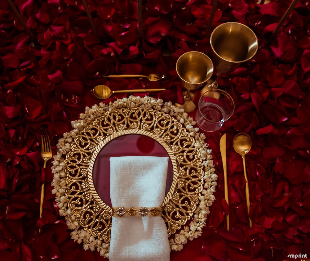 Charger Plate - Brass on red rose petals with napkin and silverware, ideal for enhancing elegant tablescapes at special events.