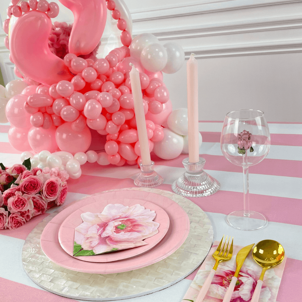 A Clear W/ Rose Charm Glass amidst a table set with pink plates, balloons, and a pink balloon sculpture. Ideal for events, adding a colorful touch to any themed party.