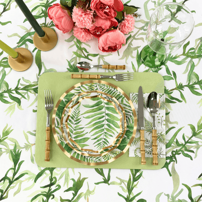 Fern &amp; Foliage Paper Guest Towel Napkins-20 Per Package displayed with a plate, silverware, and a glass on a table, complemented by pink flowers and a stack of plates with leaf designs. Ideal for adding elegance to any party setup.