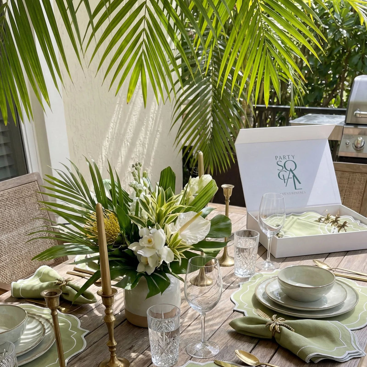 Tropical-themed table with Palm Serenity Gift Set featuring scalloped placemats, linen napkins, gold napkin rings, and elegant glassware, perfect for Ramadan gatherings.