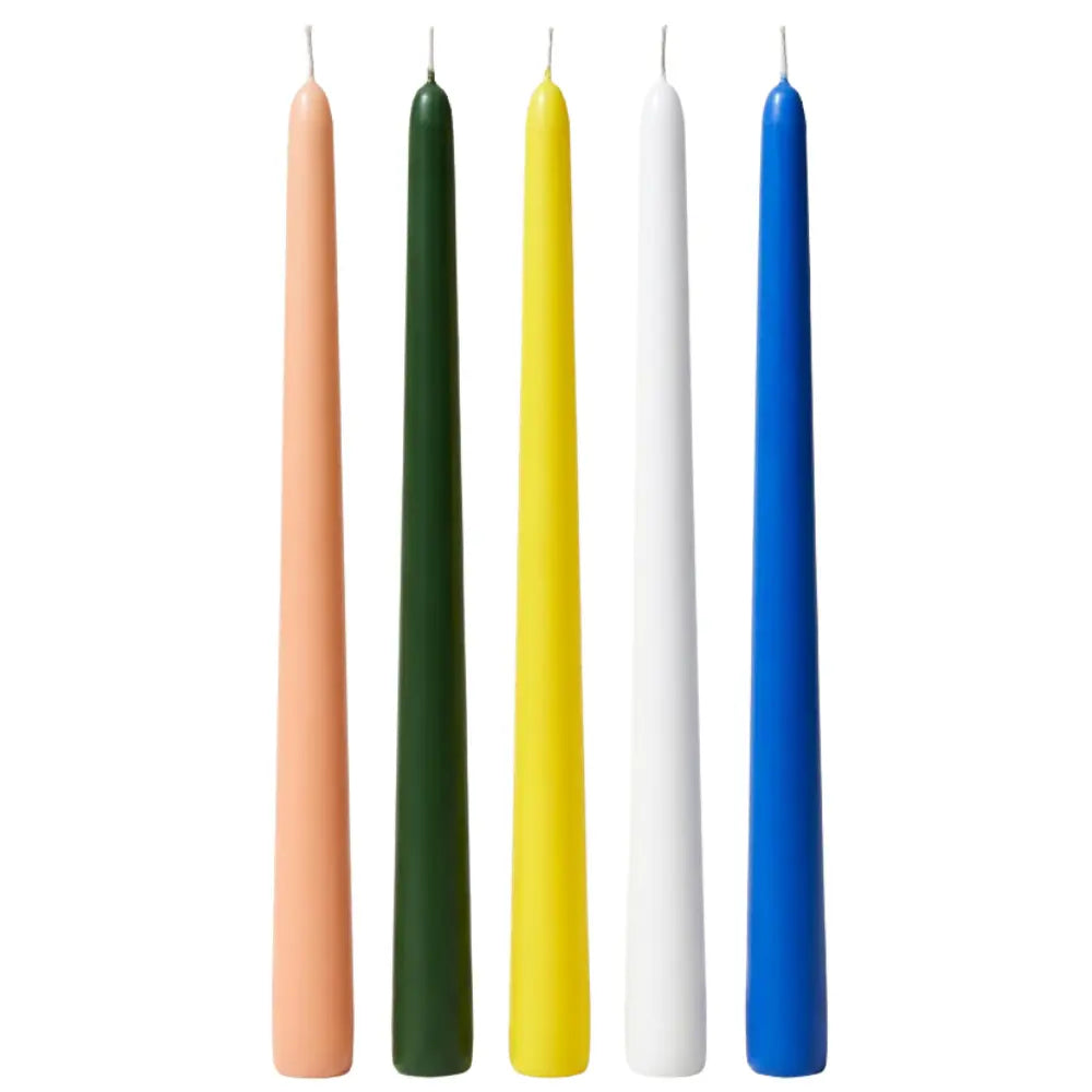 Five slim taper candles in peach, dark green, yellow, white, and blue, standing upright on a plain white background.