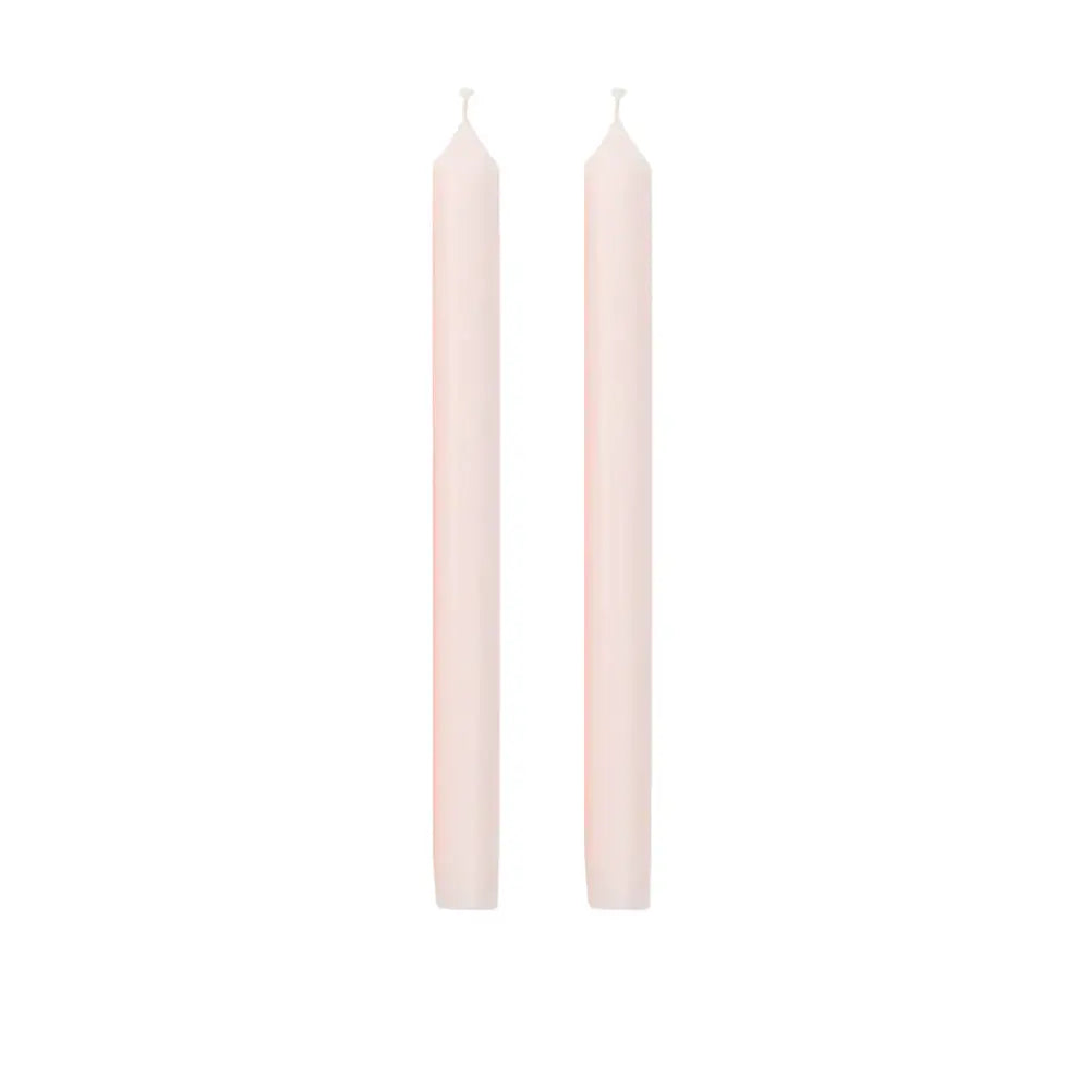 Two tall, slender taper candles in a pale blush pink color, standing upright side-by-side on a solid white background.