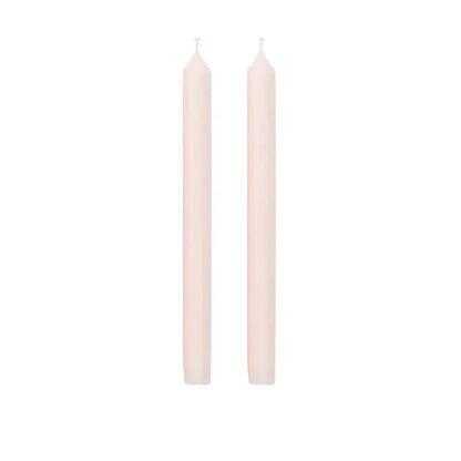 Two tall, slender taper candles in a pale blush pink color, standing upright side-by-side on a solid white background.