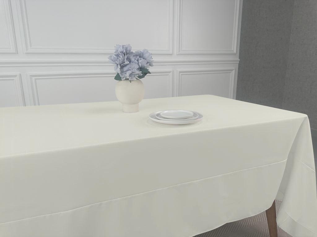 A white table with a vase of flowers, showcasing the Polycotton Tablecloth. Perfect for any event, this lightweight tablecloth adds a touch of elegance to your dining table. Easy to wash and reuse, it&