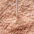 Close-up of a light sand textured carpet with a white cord or stick standing vertically in the center.