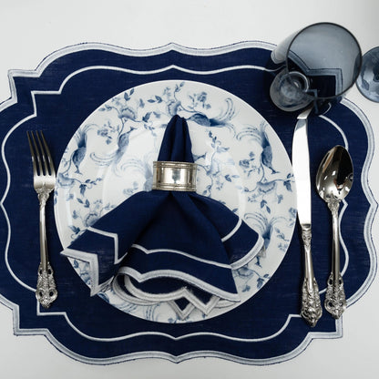 Top-down view of Navy Scalloped Linen Placemats in an elegant table setting with matching napkin, silver cutlery, and a smoky glass goblet.