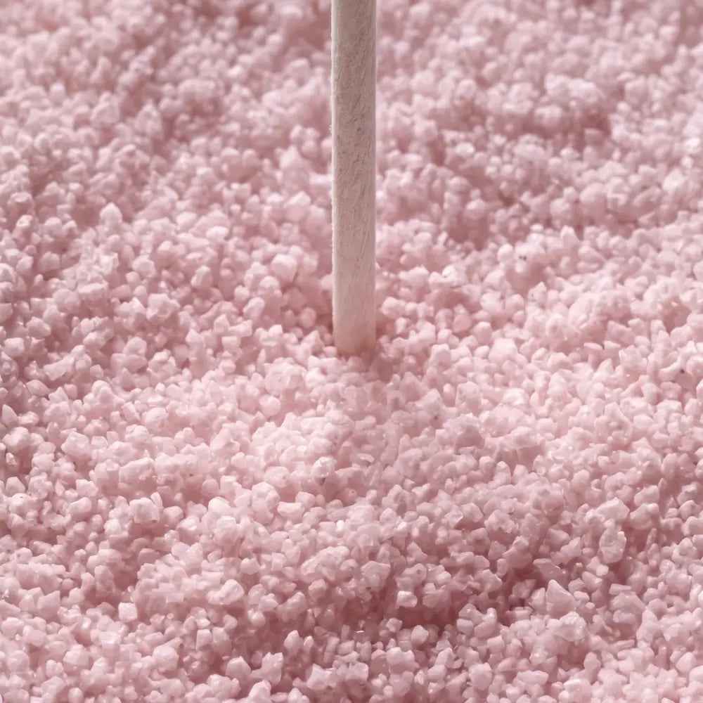 A close-up of light pink sugar crystals or sprinkles with a single white stick standing vertically in the center.