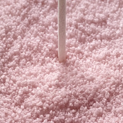 A close-up of light pink sugar crystals or sprinkles with a single white stick standing vertically in the center.