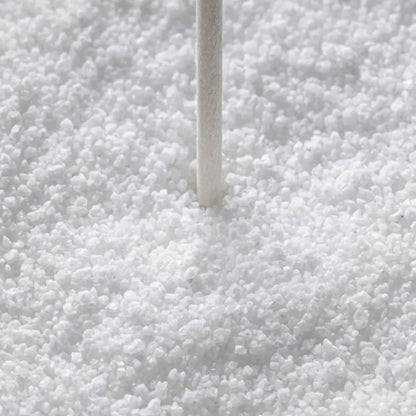 A close-up of white granular material, likely salt or sugar, with a thin white stick or rod standing vertically in the center.