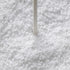 A close-up of white granular material, likely salt or sugar, with a thin white stick or rod standing vertically in the center.